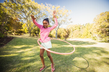 African American female child spinning pink hula hoop on grassy park lawn under sunny sky © wavebreak3
