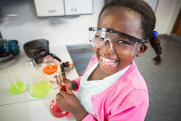 African American girl mixing red solution with dropper in school science lab, showing bright flasks