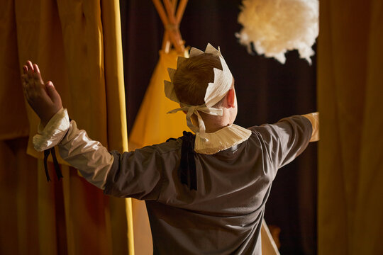 Rear view of little boy wearing kings costume with paper crown entering scene while performing on stage of childrens theater during fairytale play