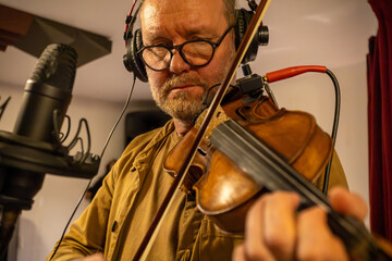 A man plays the violin in a recording studio, using a professional condenser microphone.