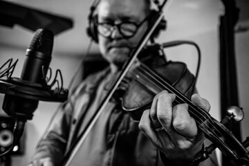Black and white image of a man playing the violin in a recording studio, using a professional condenser microphone. © Christo