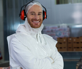 Man wearing coveralls apron and earmuffs standing arms crossed in processing plant, copy space