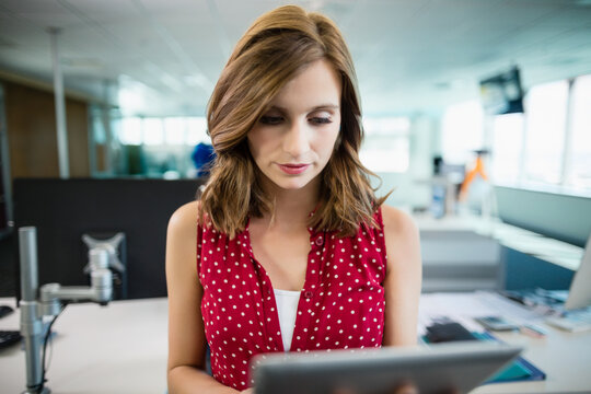 Woman standing at desk in modern open-plan office, using tablet with focused expression