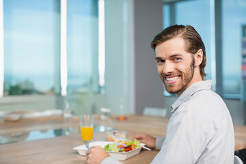 30s male eating salad from takeout box and drinking orange juice at office cafeteria, copy space