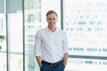 Man standing in modern office by glass windows, with potted plant and city building cross-brace