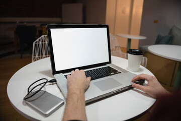 Man typing on silver laptop at white table in cafe, with external drive and coffee cup