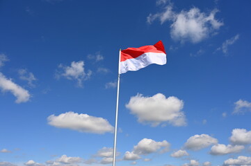 The Indonesian flag flutters in the wind in a blue sky with white clouds