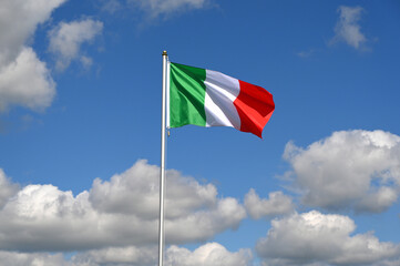 The Italian flag flutters in the wind in a blue sky with white clouds