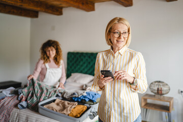 mother use mobile phone, while daughter pack clothes to suitcase