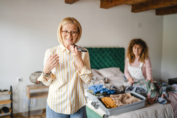 mother use mobile phone, while daughter pack clothes to suitcase