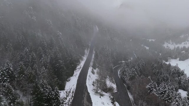 Mountain road winding through snow-blanketed forest, aerial perspective revealing scenic winter landscape under overcast sky