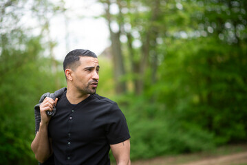 Hispanic male adult in nature wearing black shirt and carrying jacket