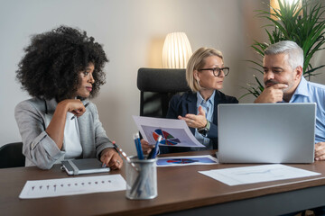 Three busy happy middle aged professional business man and two women executive leaders team using laptop working on computer at work desk having conversation on financial project at meeting in office.