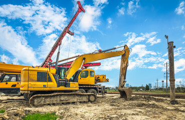 Yellow crawler excavator with digging bucket parked at muddy construction site under blue sky.
