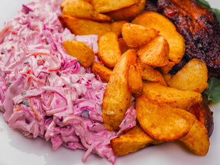 Simple meal with pork belly, potato wedges and pink coleslaw on white plate. Fine dinner with simple products.
