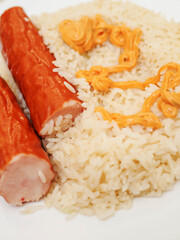 Dinner meal with rice and two sausages and orange color sauce on light color table cloth. Simple tasty food.