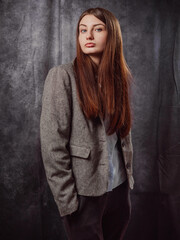 Fototapeta premium A young business woman is wearing a gray jacket and black pants. The model has long brown hair is elegant and is standing in front of a gray color background. Lady boss concept. Classic portrait.