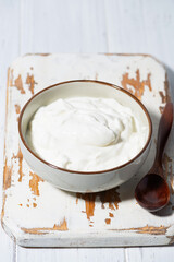 greek yogurt in a white bowl on a wooden board, vertical