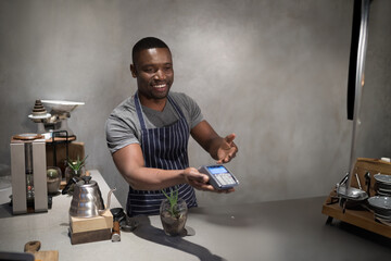 African American man handing over payment terminal in coffee shop, with coffee grinder, scale, cups