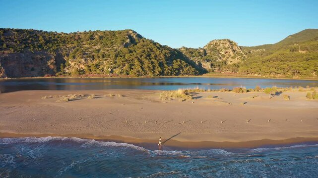The peaceful atmosphere of Iztuzu Beach is captured in this impressive shot, where a drone slowly rotates as it follows a woman walking along the shore.
