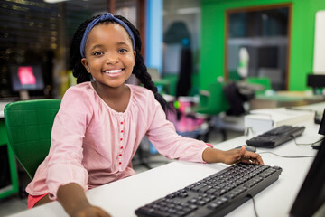 Teenage African American girl sitting at white desk in modern lab, reaching toward black keyboard