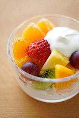 Colorful summer fruit salad in a clear glass bowl topped with creamy yogurt, ideal for healthy snacking and sunny day gatherings
