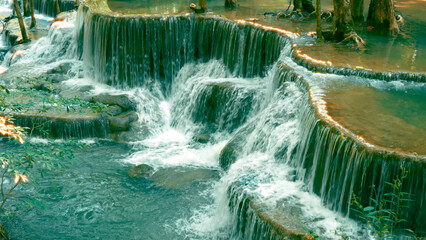 Scenic view of multi-tiered waterfall cascading over rock formations in lush green forest with flowing water creating serene and natural landscape