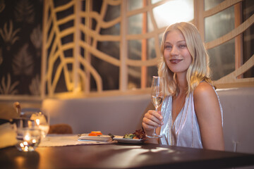 Woman sitting in restaurant booth, holding champagne flute with salad and ice bucket, copy space