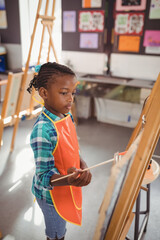 Obraz premium African American child painting on easel in art classroom, with paintbrush and canvas, copy space