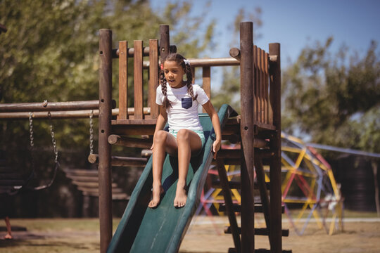 Girl child sliding down green plastic slide in park playground, enjoying sunny outdoor fun