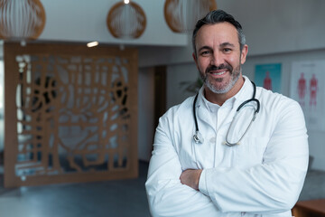 Middle-aged male doctor standing in clinic reception, wearing lab coat with stethoscope, copy space