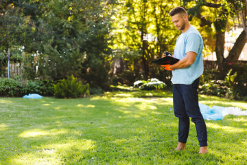 Man taking notes with black clipboard and pen wearing orange glove in backyard garden, copy space