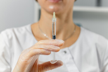 A nurse or doctor holds an injection needle and a hypodermic injection in her hand, extended...