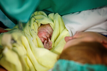 Newborn baby wrapped in blankets after birth. Mother looking for the first time on new born...