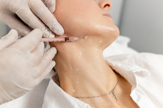 Hands of a beautician during biorevitalization or botulinum therapy of the skin of a woman's neck - close-up 