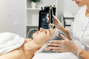  Young woman undergoing radio frequency facelift procedure. Concept of advertising facial skin care, anti-aging facial rejuvenation. Radio wave facelift in cosmetology clinic. RF lifting
