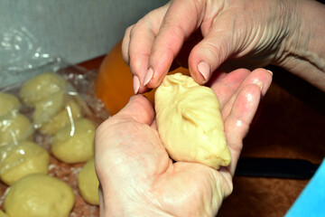 The picture shows women's hands forming a bun with filling from yeast dough.