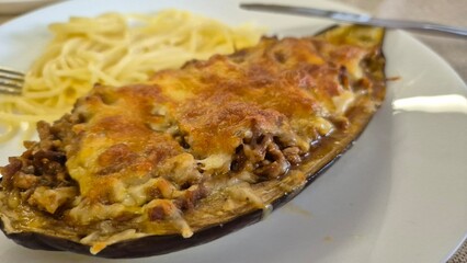 Stuffed eggplants with ground veal and melted cheese baking in a glass dish. A delicious homemade meal being prepared for lunch or dinner in a home kitchen.