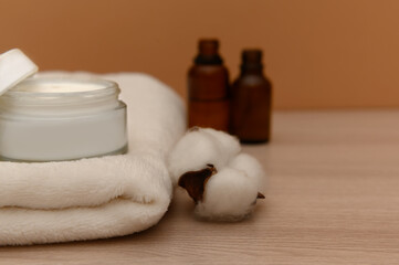 There is cosmetic cream and white cotton on a white towel.