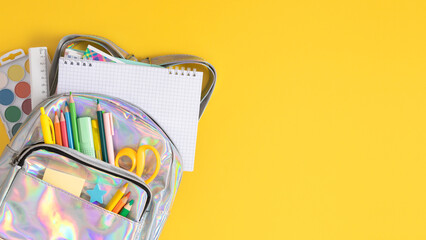 Back to school concept. Bright backpack filled with colorful school supplies on yellow background. Perfect for educational themes and stationery marketing. Top view.