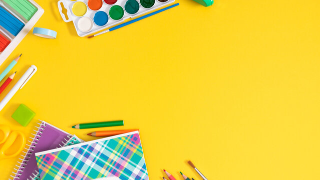 Back to school concept. Frame made of colorful school supplies, paints, plasticine, notepad, scissors, pens, sharpener on a yellow background. Flat lay, top view, copy space.