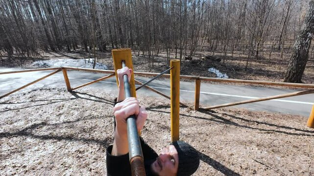 A physically fit individual engages in a challenging workout session performing pullups on a sturdy bar set in a peaceful forest environment that beautifully blooms during early spring