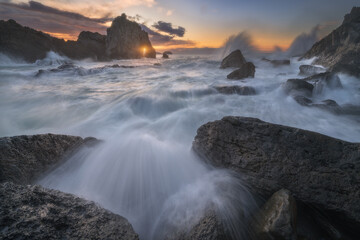 Sunset at the rocky coast of Laga beach in Bizkaia, northern Spain, with strong waves crashing against the rocks of the Cantabrian Sea