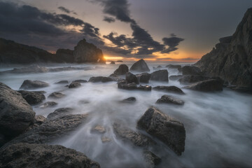 Obraz premium Sunset at the rocky coast of Laga beach in Bizkaia, northern Spain, with strong waves crashing against the rocks of the Cantabrian Sea