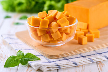 cheddar cheese sliced ​​into cubes in a clear glass bowl on a kitchen table, selective focus.
