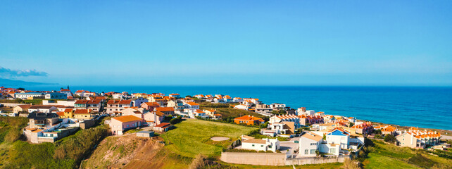 Aerial view of a small European town against blue sky and Atlantic Ocean. Drone view of a beautiful European city with a hilly landscape on ocean background. Beautiful natural landscape. Portugal.