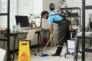 Man in uniform cleaning floor with mop in office