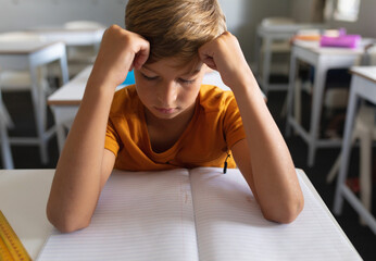 Schoolboy sitting at desk in classroom, focusing on open notebook and yellow ruler