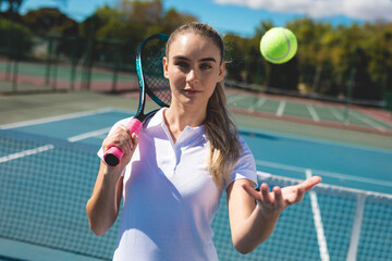 Female tennis player holding racket with pink grip, tossing ball near net on court, preparing serve