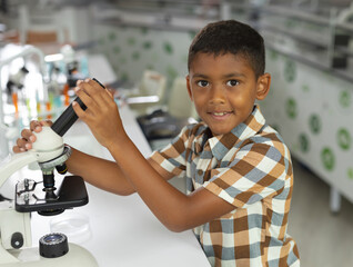 Boy adjusting light microscope eyepiece in school science lab, handling petri dish and glassware